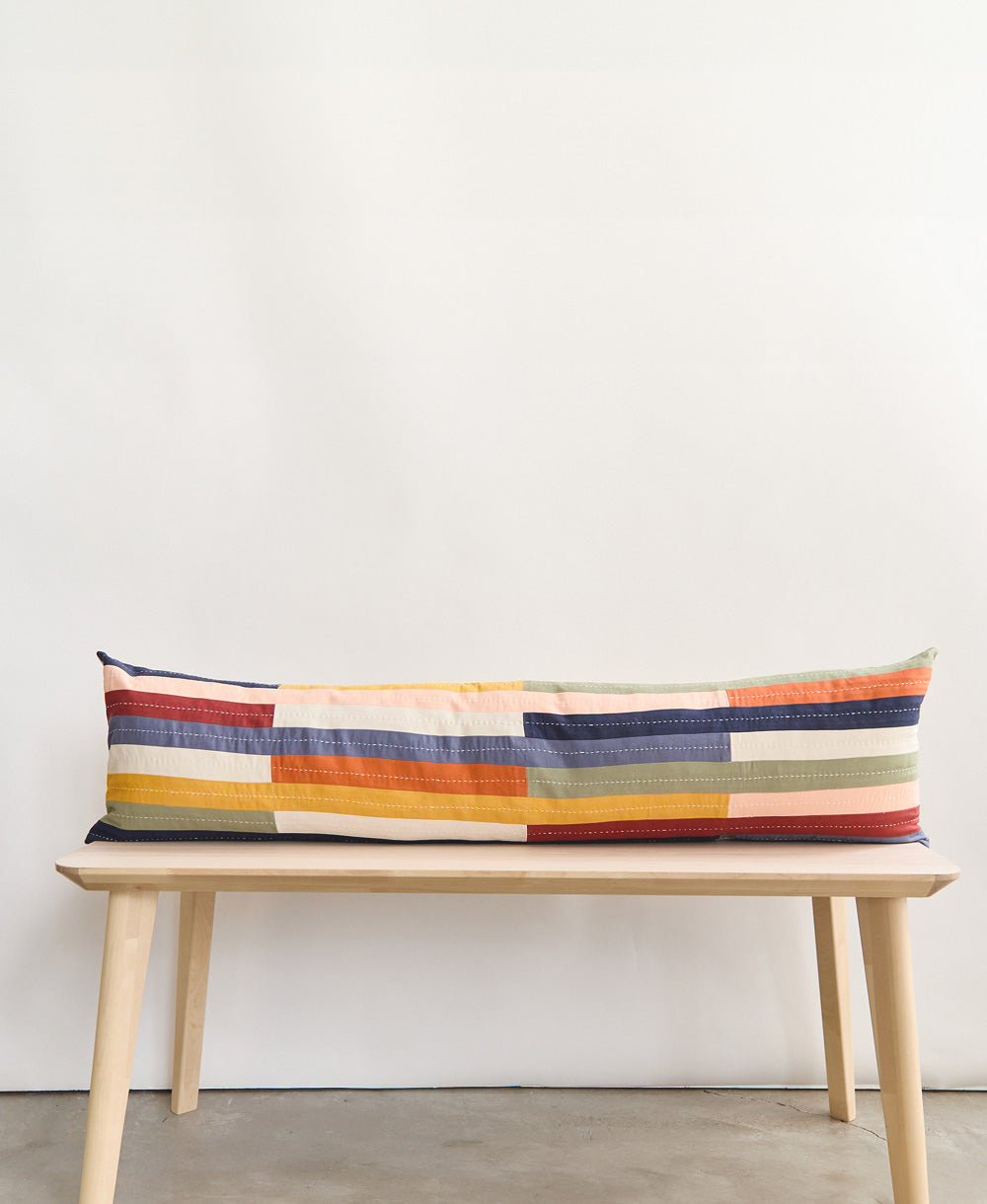 Cojín lumbar largo Rainbow sobre una banca de madera